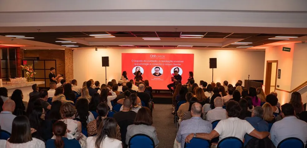 Auditório cheio na OritCON'26, com o telão do painel O legado do cuidado ao fundo